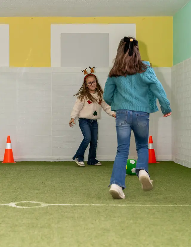 Duas crianças a jogar à bola no campo de relva sintética.