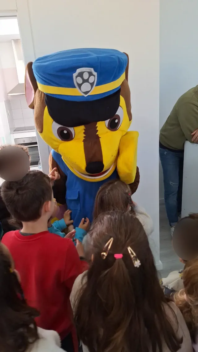 Mascote de cão-polícia rodeado de crianças numa festa.
