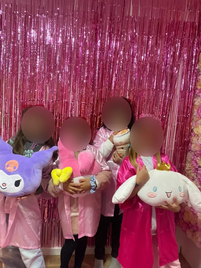 Meninas de roupão de cetim cor-de-rosa, com peluches, numa festa spa. As caras estão desfocadas.