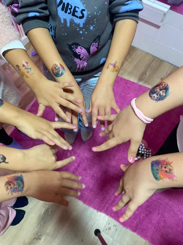 Mãos e braços de várias crianças com tatuagens temporárias coloridas, numa festa.