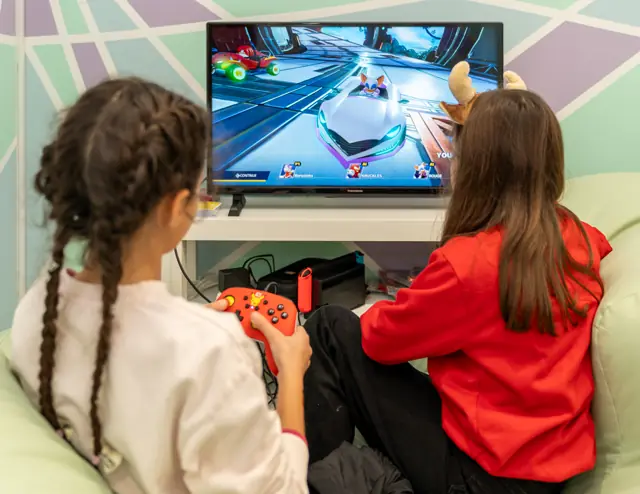 Duas meninas a jogar consola em frente à televisão.
