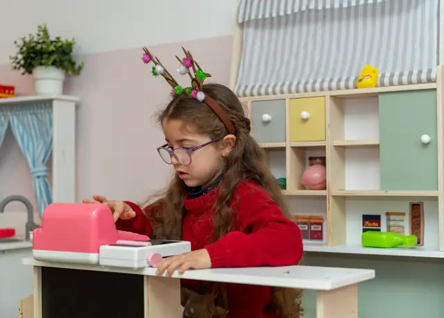 Menina com bandolete de rena a usar a caixa registadora da Lojinha.