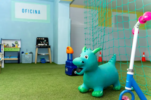 Oficina com bancadas de ferramentas de brincar e um cavalinho saltitão na relva.