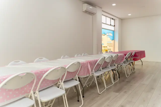 Sala da festa com mesa comprida e cadeiras preparadas para o lanche.